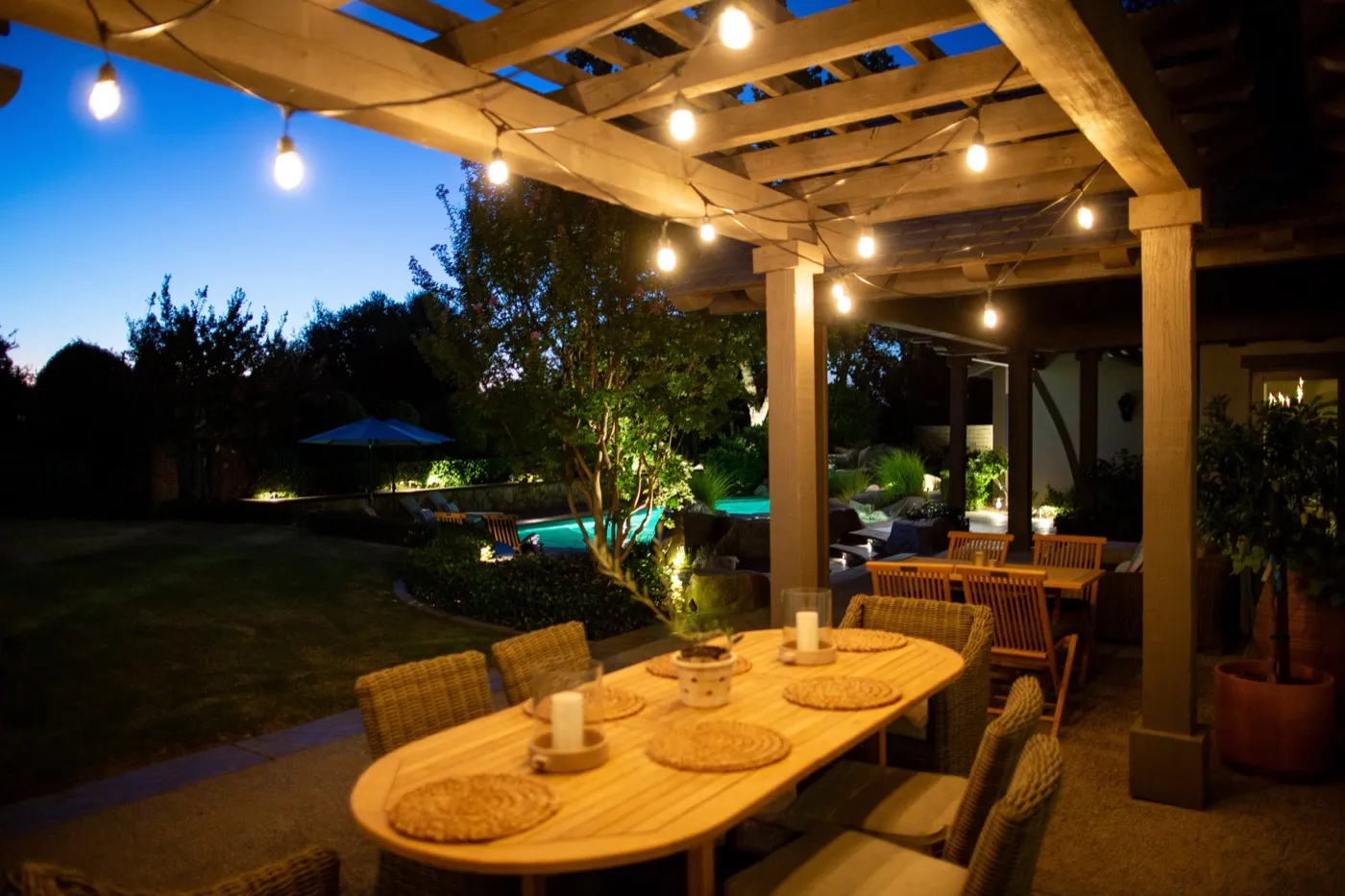 Covered patio dining area with string lights and landscape lighting beyond