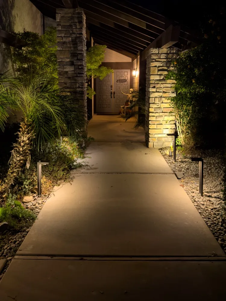 Warm path lights illuminating a narrow concrete walkway beside stone walls and planting
